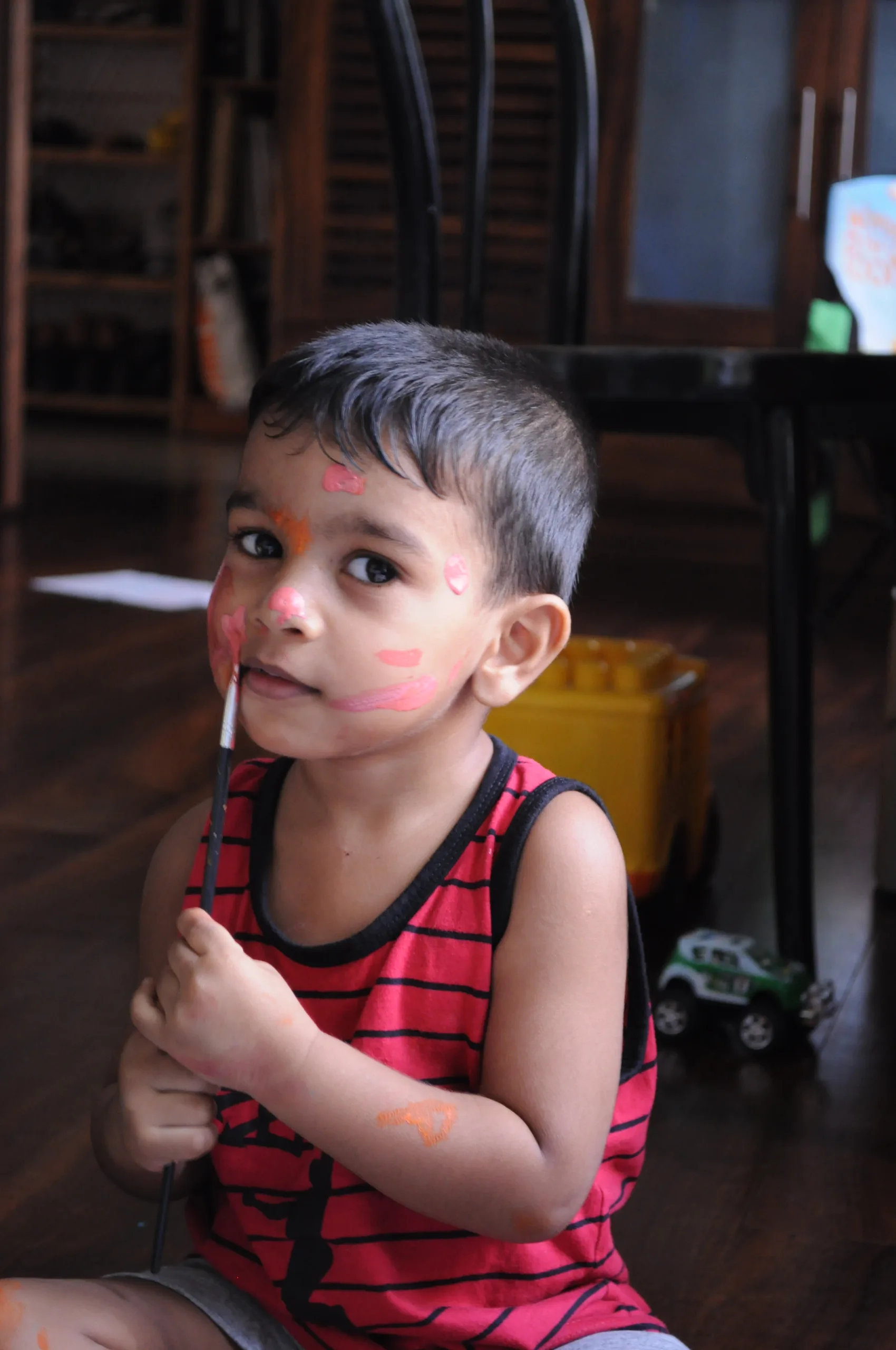 A child with face paint holding a paintbrush